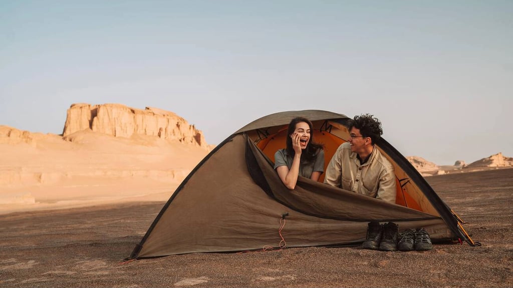 A Happy Couple Enjoys A Peaceful Moment In A Tent Amidst The Rugged Beauty Of Lut Desert, A Perfect Setting For **Budget Your Trip To Iran** While Experiencing The Country'S Natural Wonders.